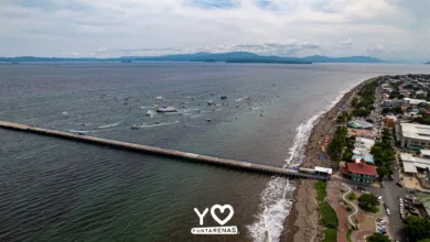 Vista aérea de Puntarenas durante la procesión marítima de la Virgen del Mar, con embarcaciones frente al muelle y la playa.