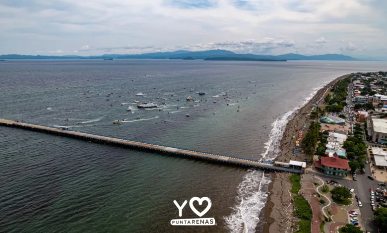 Vista aérea de Puntarenas durante la procesión marítima de la Virgen del Mar, con embarcaciones frente al muelle y la playa.